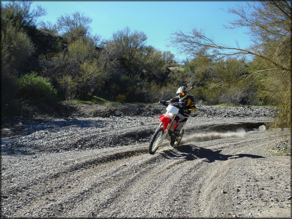 Rider wearing black and yellow Thor motocross gear on Honda CRF250X going through gravel wash.