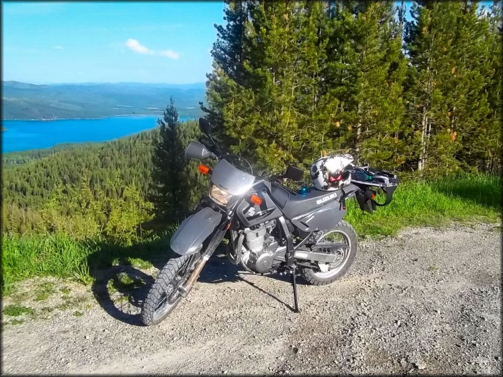 A dual sport Suzuki motorcycle with helmet and rider pack parked next to Ashley Lake.