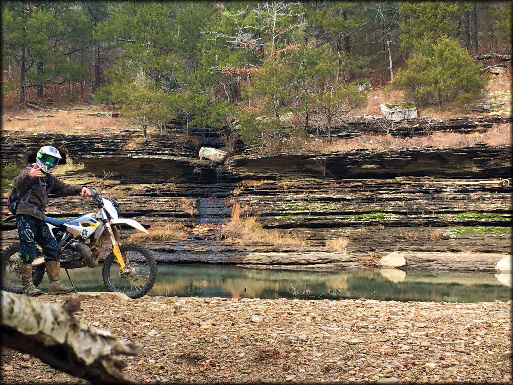 Husqvarna motorcycle and rider posing near a small waterfall on the trail.