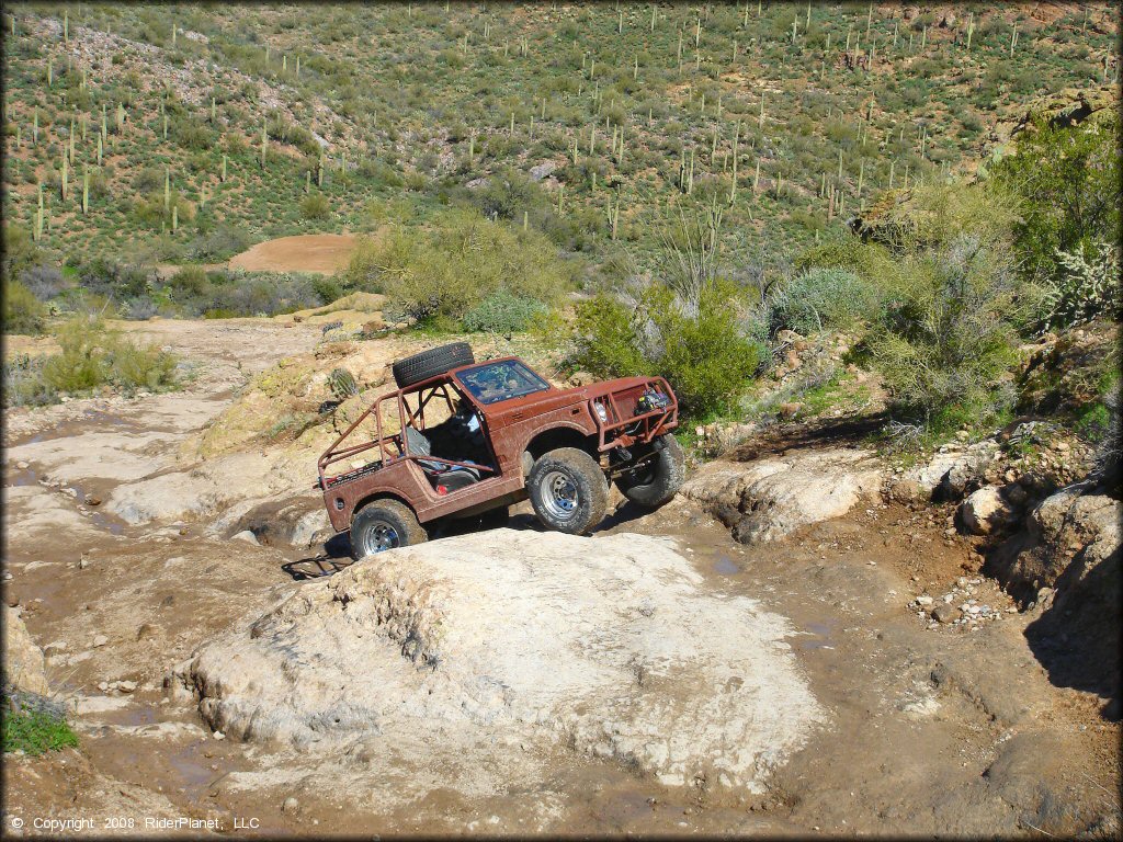 Modified Suzuki Samurai with sprare tire on the roof crawling up rocky boulder.