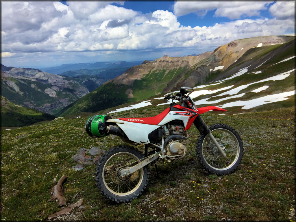 A Honda CRF 230 with a green motorcycle helmet on the exhaust pipe in the rocky mountains.