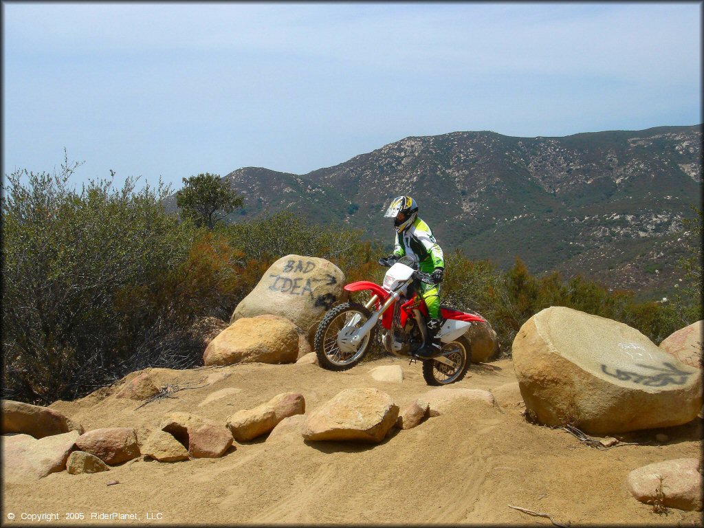 Man on Honda CRF250X riding through big rocks on trail.