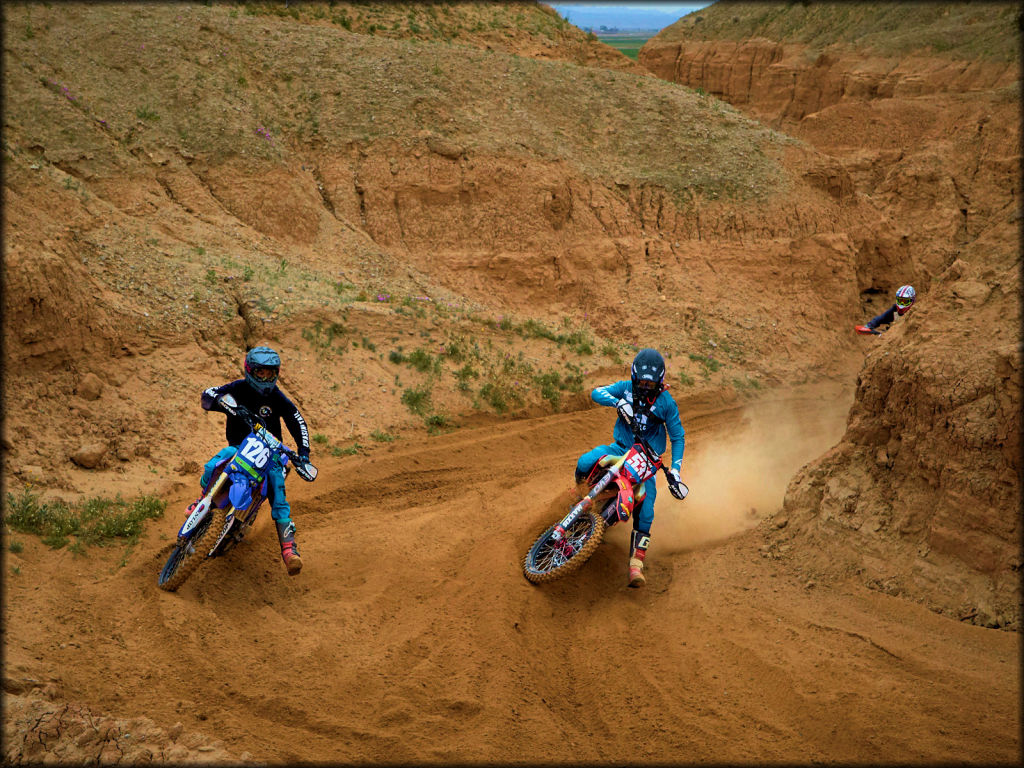 Three Motocross Bikes Railing a Small Berm in a Narrow Canyon