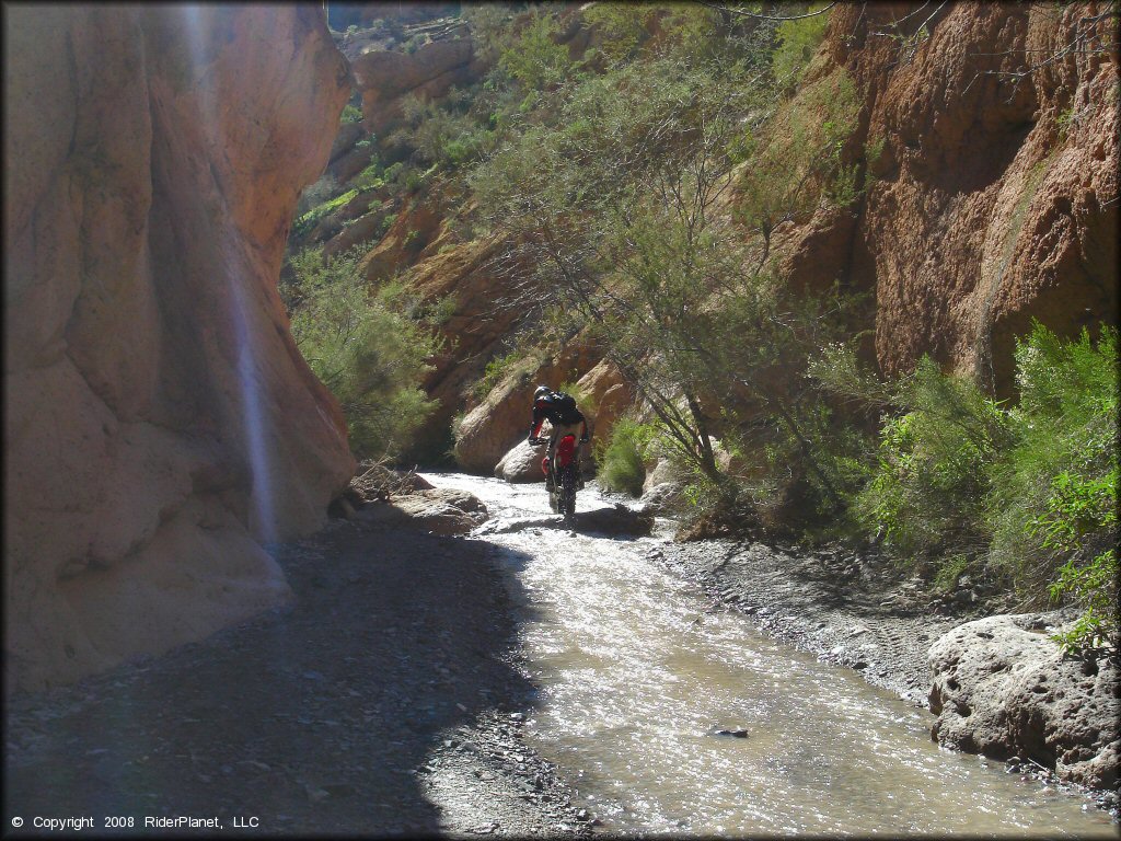 Honda dirt bike riding though box canyon with shallow stream.