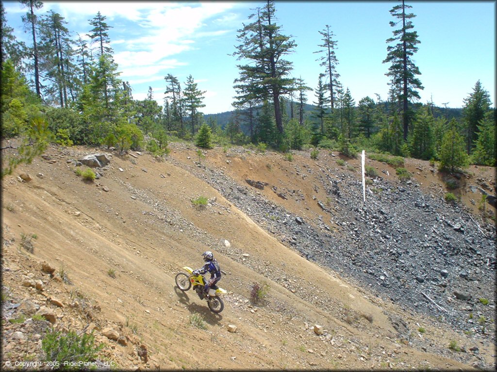 Suzuki RM 100 two-stroke dirt bike going up small gravel hill.