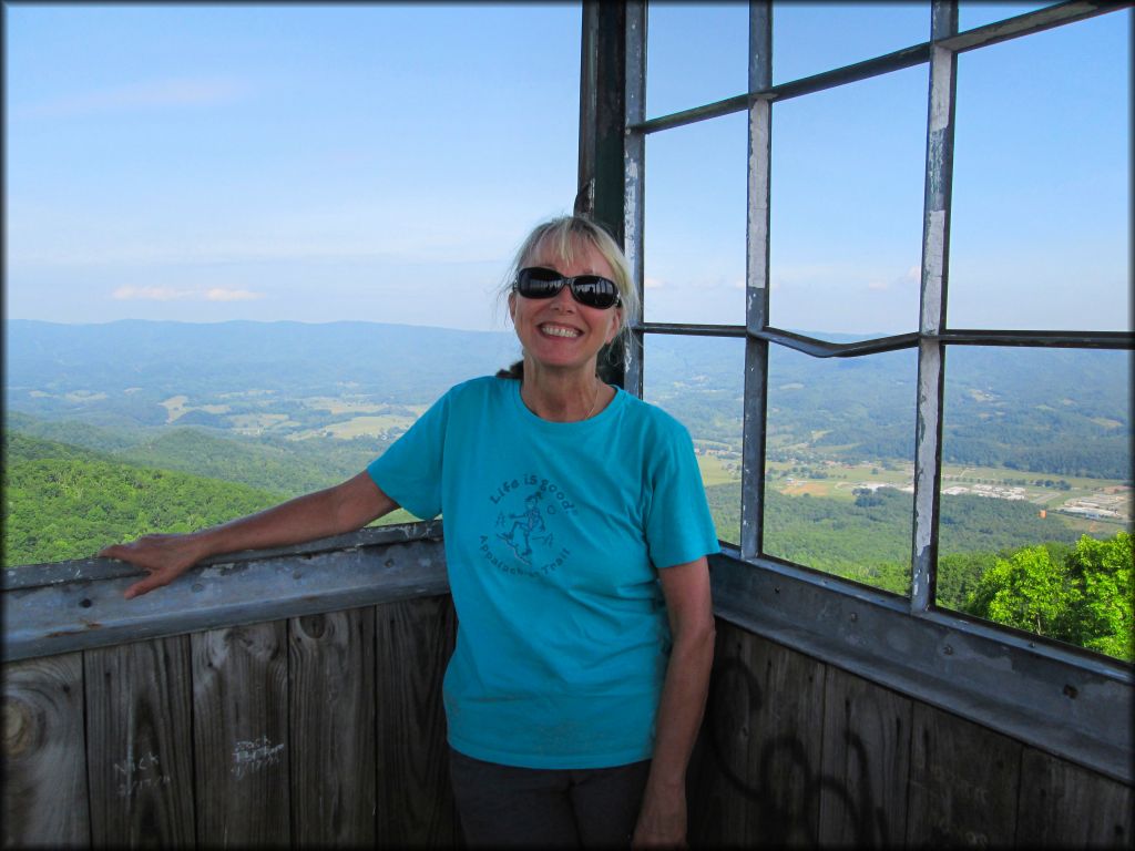 Photo of mature woman with scenic views of valleys, forest and hills taken from top of fire tower.