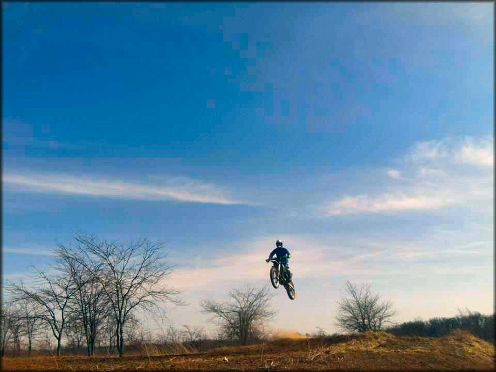 Kawaski dirt bike and rider jumping on motocross track.
