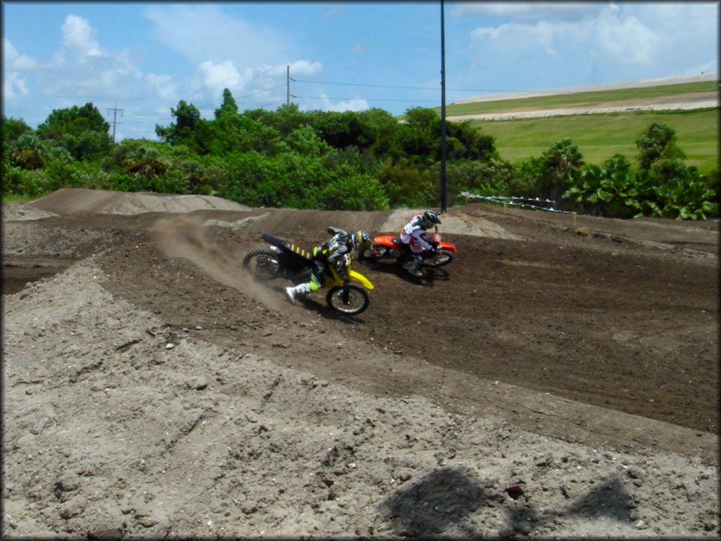 Suzuki and Honda dirt bikes riding though deep berm on motocross trackk.