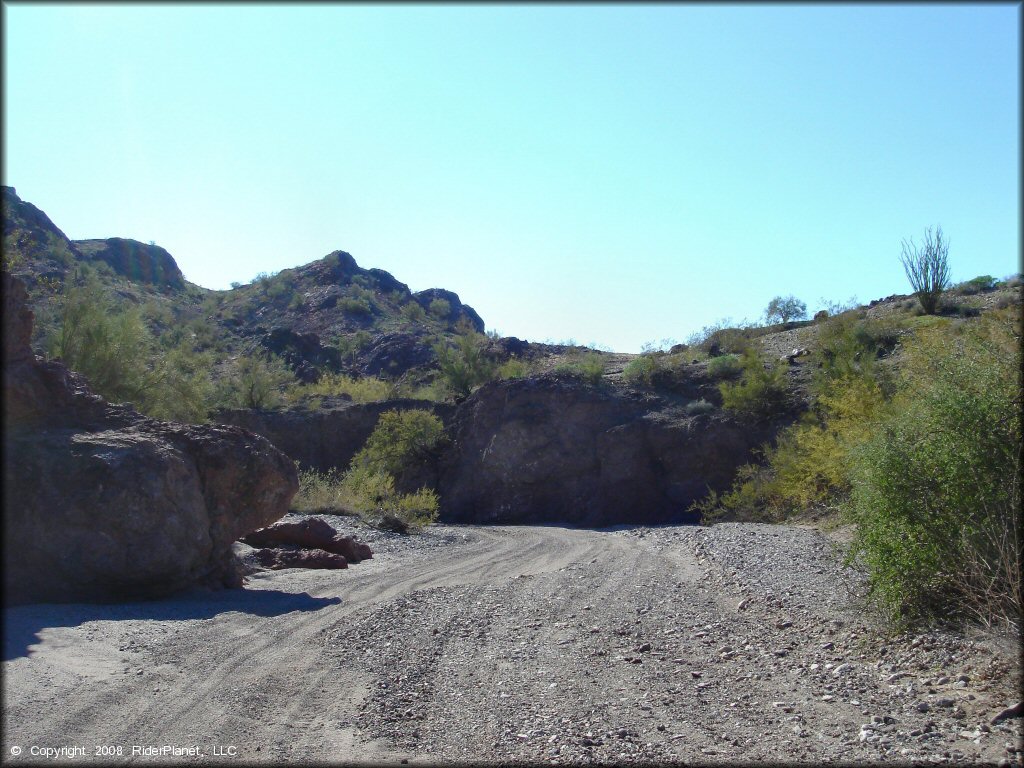 A section of sandy wash surrounded by rock boulders and desert scrub brush.