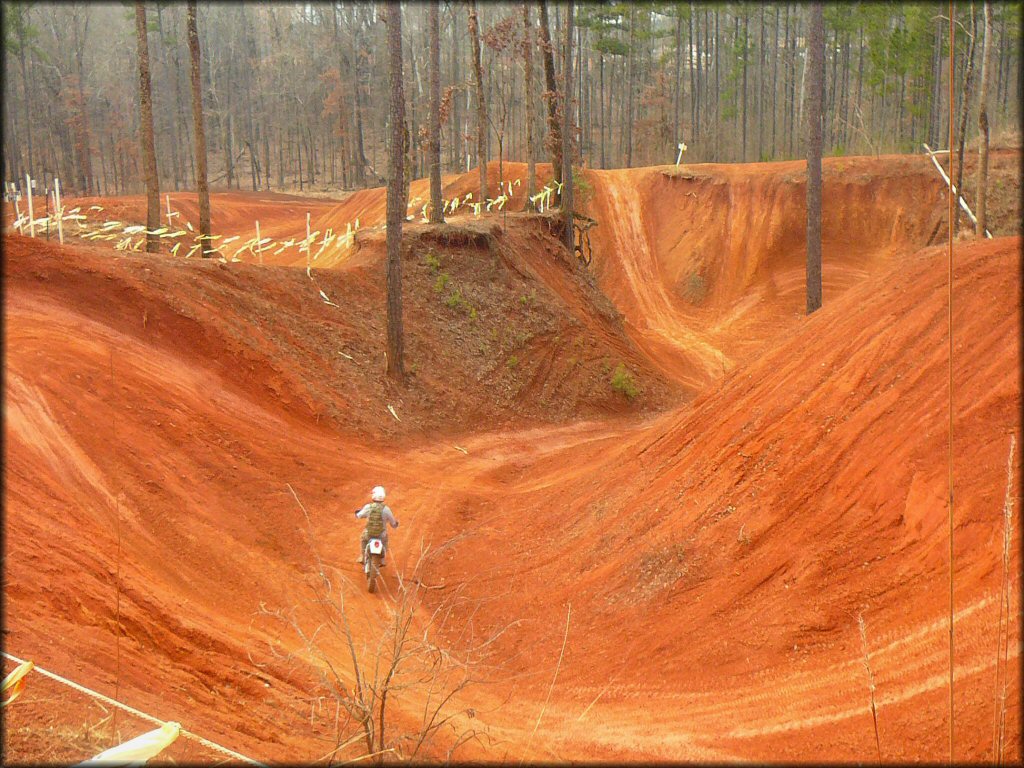 Man on dirt bike riding around the bottom of large reddish colored play pit with hill climbs and jumps.