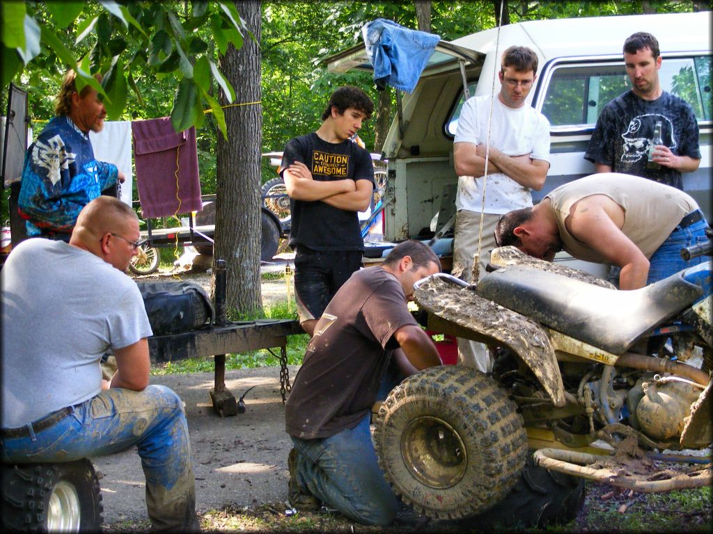 Group of young men at campsite watching an ATV being repaired.