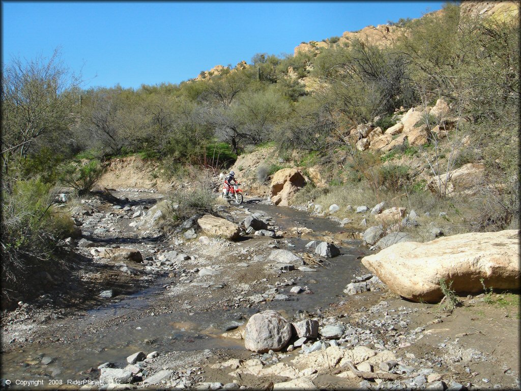 Honda dirt bike going through rocky section of shallow stream.