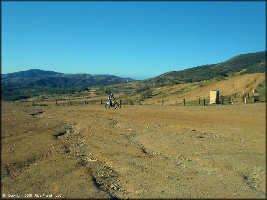 Woman on RM-250 dirt bike riding around staging area.