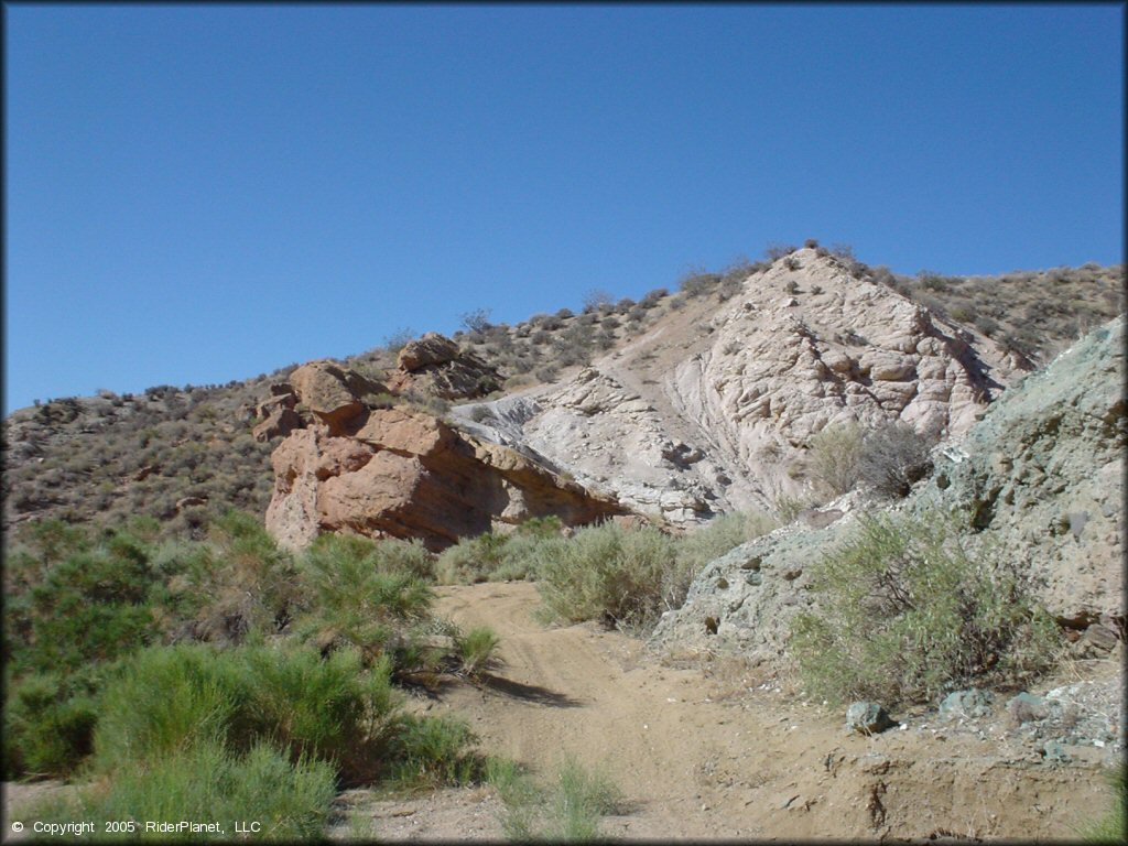 Scenic photo of sandy ATV trail winding near a large rock boulder.