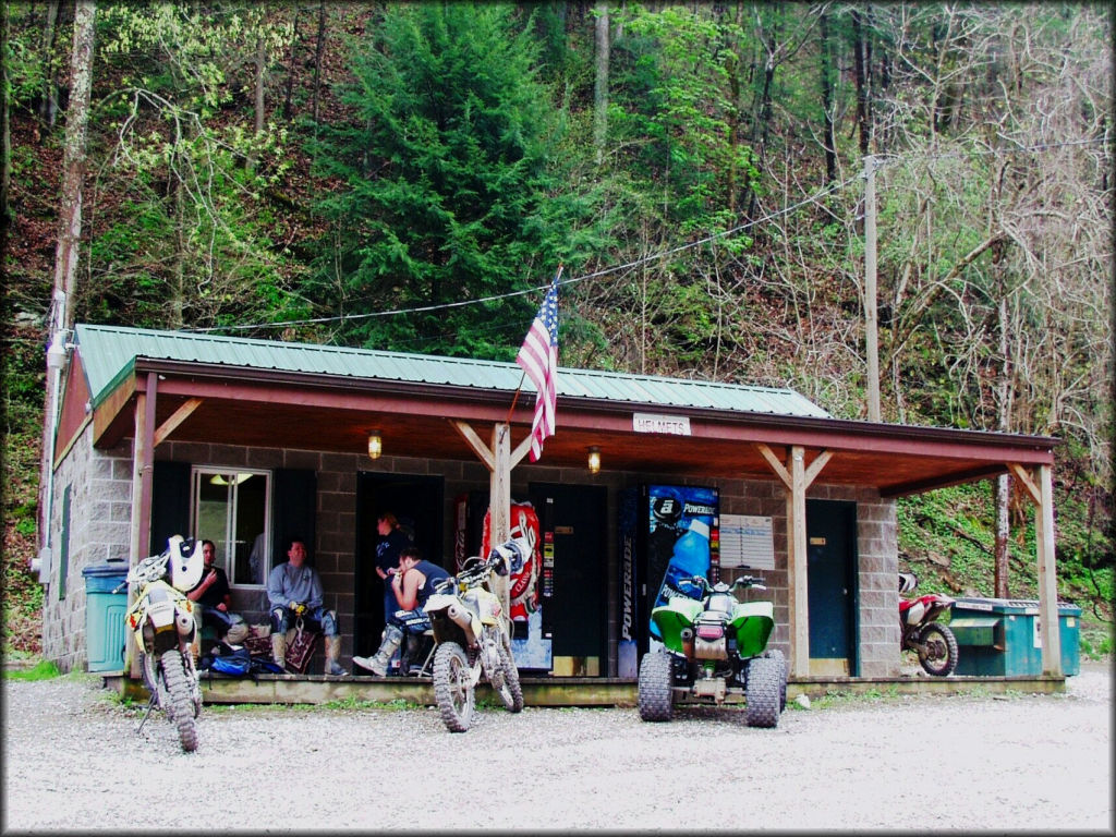 Group of trail riders sitting in front of two Suzuki dirt bikes, one Honda dirt bike and a Kawasaki quad.