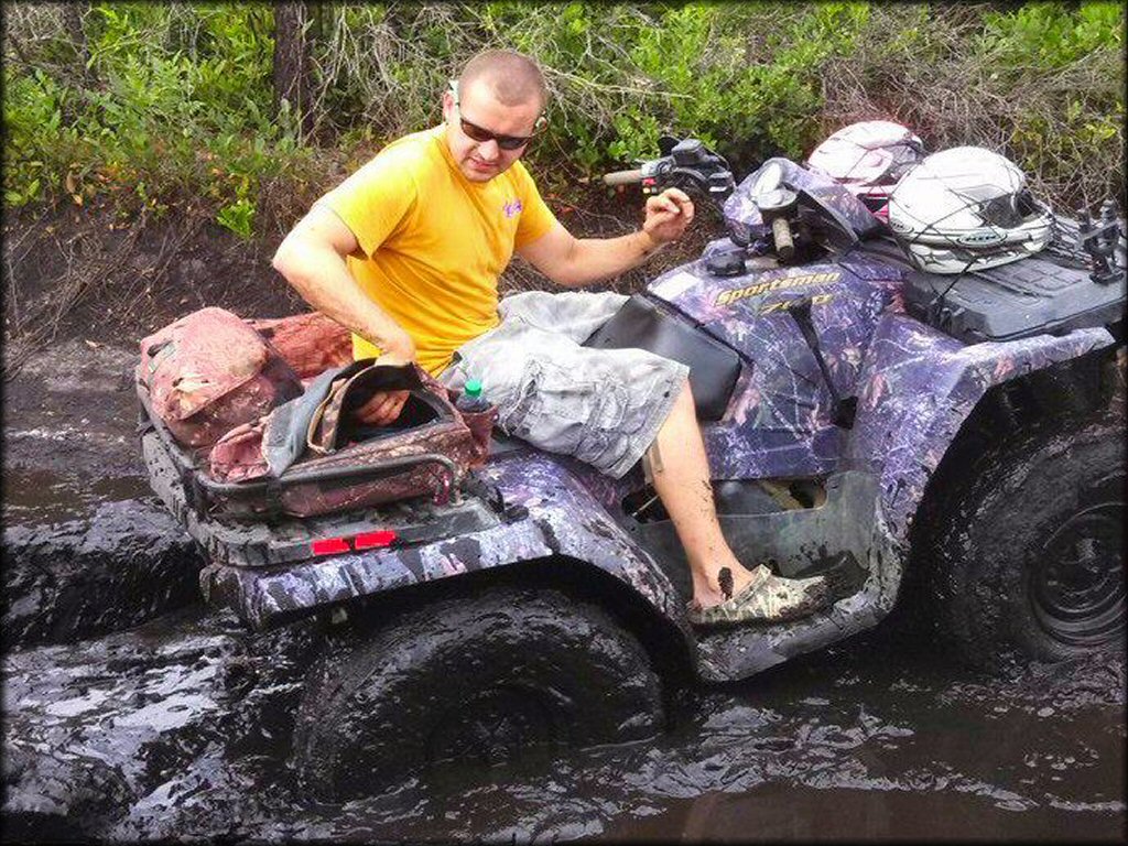 Young man sitting on Polaris Sportsman 4x4 ATV with camoflauge plastic carrying two motorcycle helmets tied to the front.