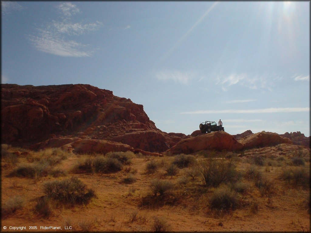 Jeep with with a spare tire on the back parked on top of large rock boulder.