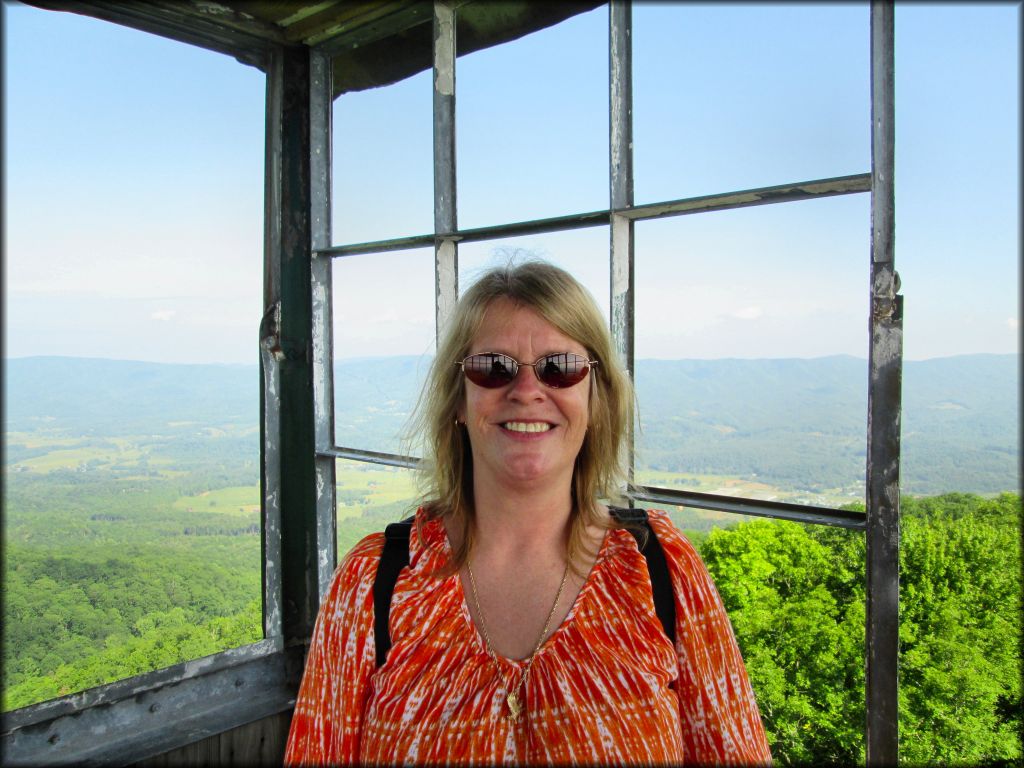 Photo of mature woman with scenic views of valleys, forest and hills taken from top of fire tower.