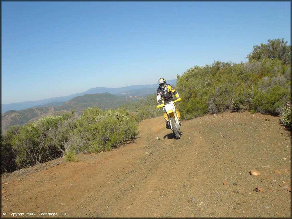 Man on Suzuki RM-250 dirt bike traveling down hard packed 4x4 trail.