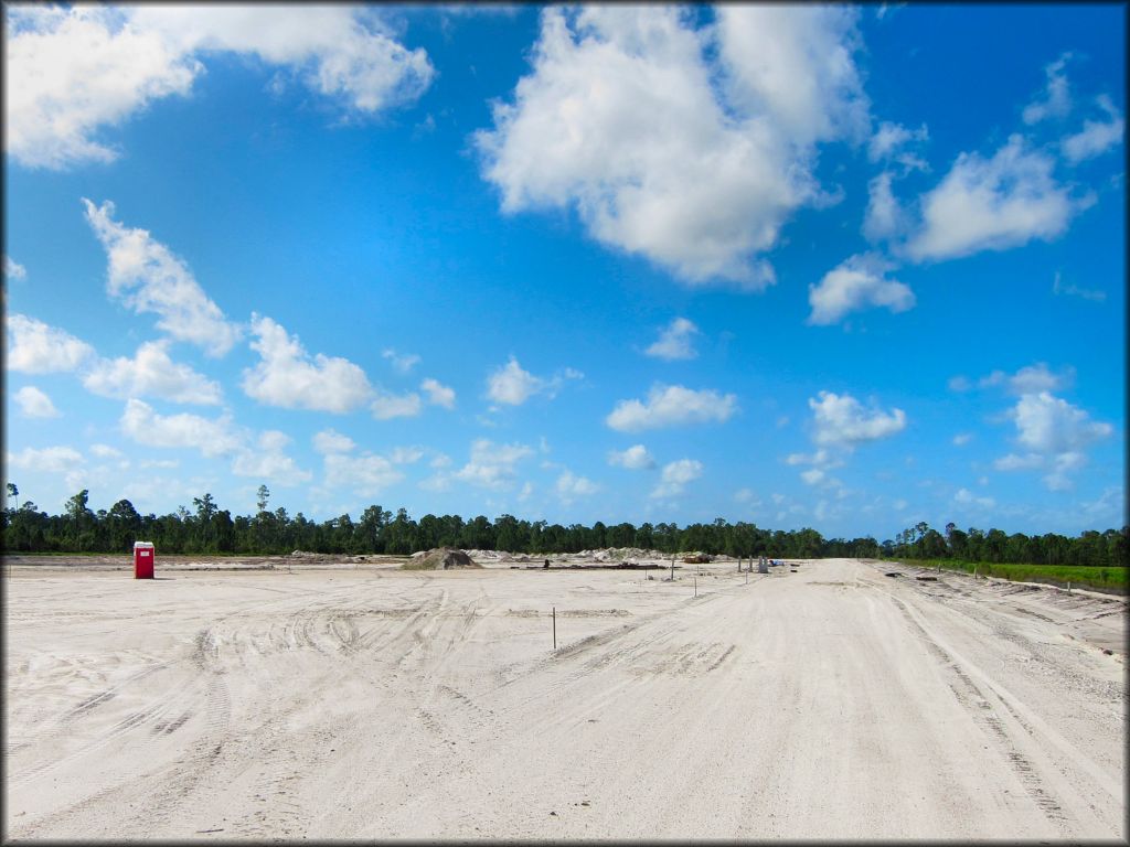 View of park main entrance road with chem toilet and mounds of dirt in the background.