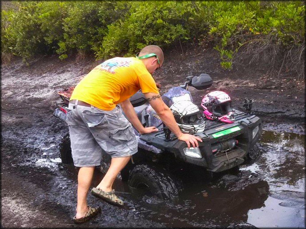 Young standing next to Polaris Sportsman 4x4 ATV with camoflauge plastic carrying two motorcycle helmets and winch in the front.