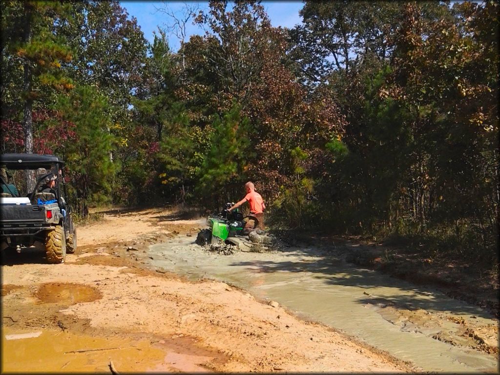 Green ATV with snorkel kit going through deep mud puddle.
