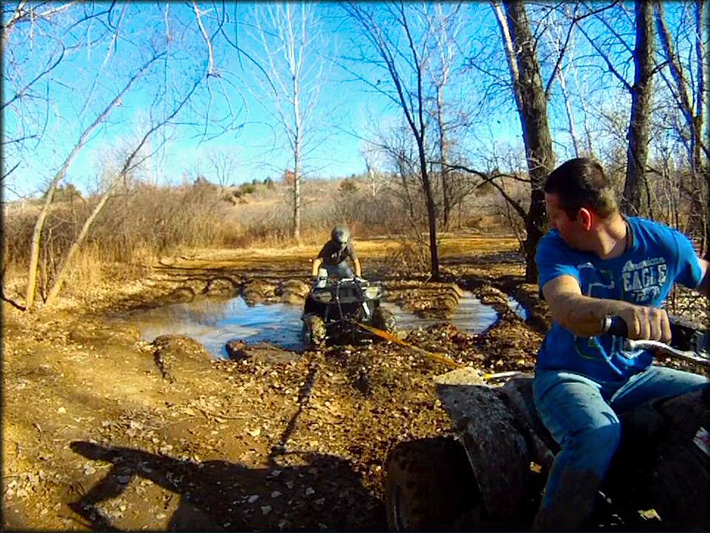 Young man using a tow rope to help pull ATV from deep mud puddle.