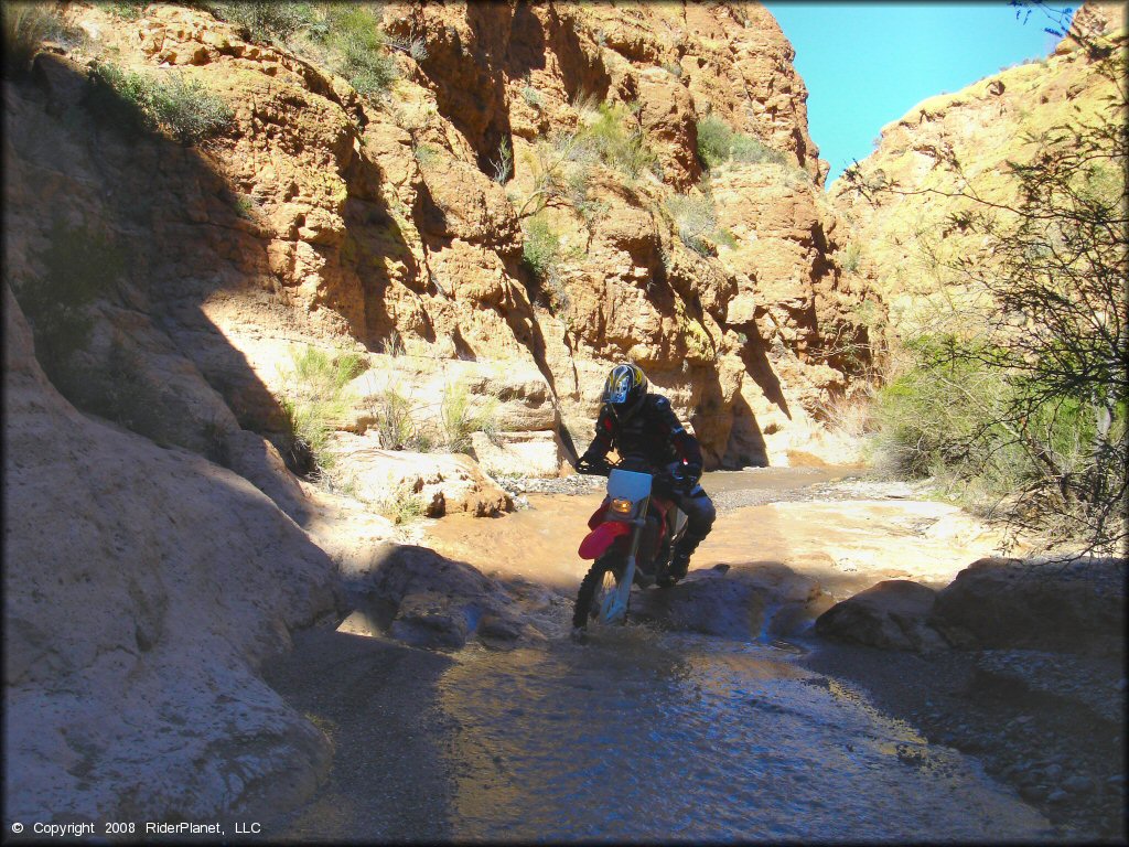 Honda CRF250 going over river rock in shallow stream.