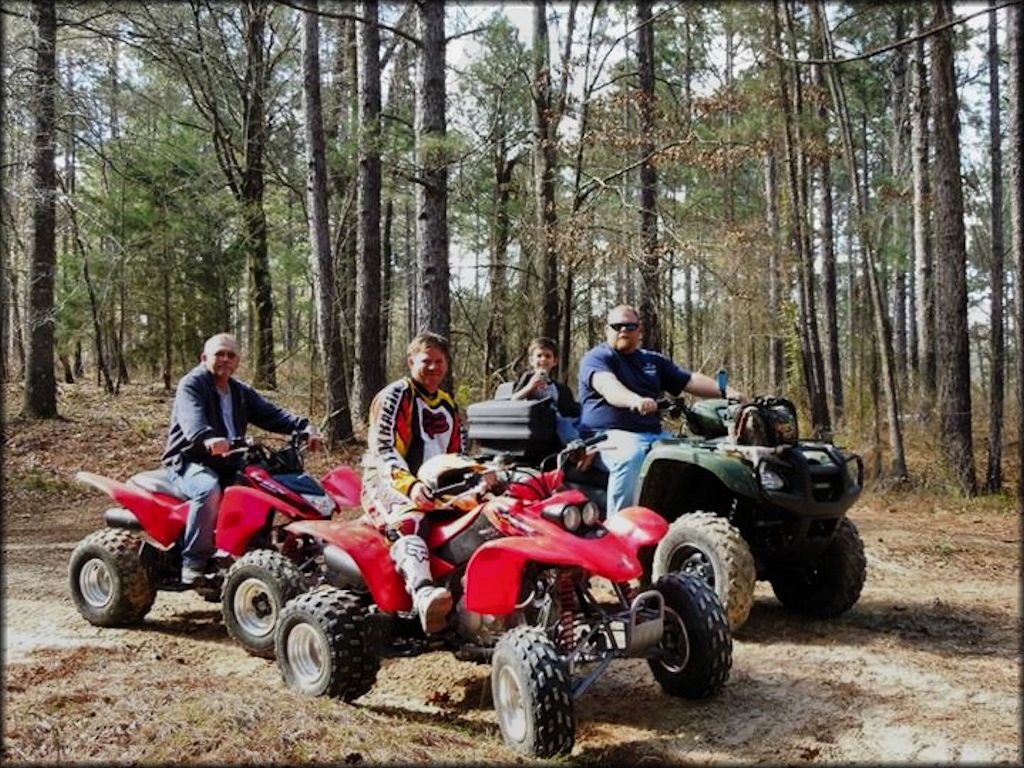 Group photo of three men and one small child each sitting on a four wheeler.
