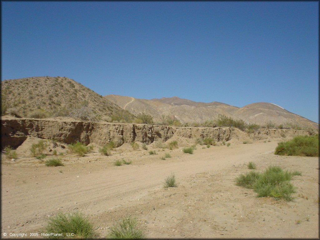 A scenic portion of a hard packed desert trail surrounded by barren rolling hills.