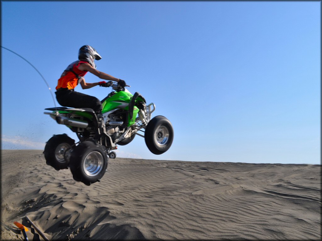 Kawasaki ATV with rear sand paddle and front sand tires catching some big air at the dunes.