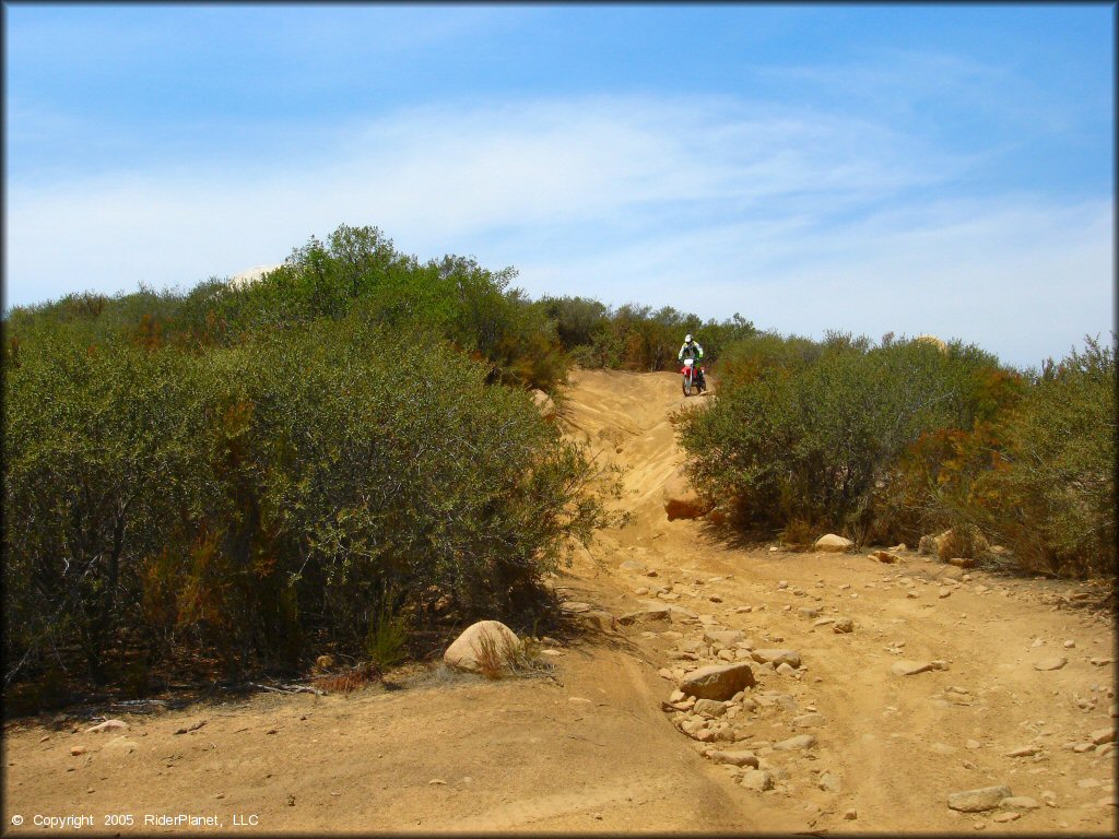 Rugged section of ATV trail with loose chunk rock and ruts.