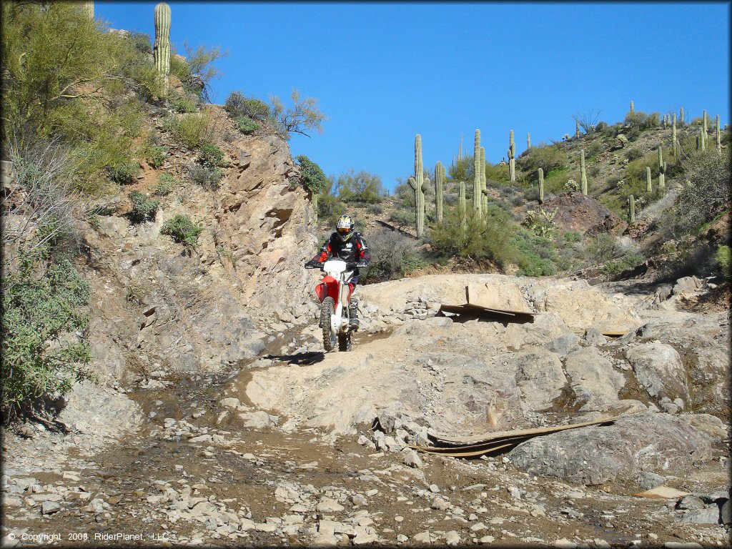 Man riding CRF-250 dirt bike going down rocky ledge.