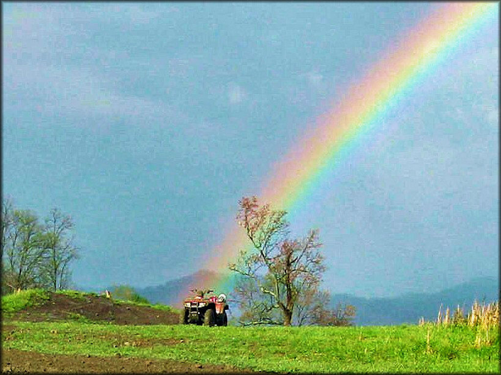 Red four wheeler parked in grassy meadow with rainbow in background.