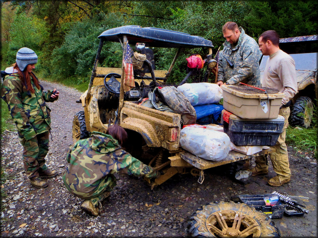 Two men and two women using tools to repair the wheel and suspension of a UTV.