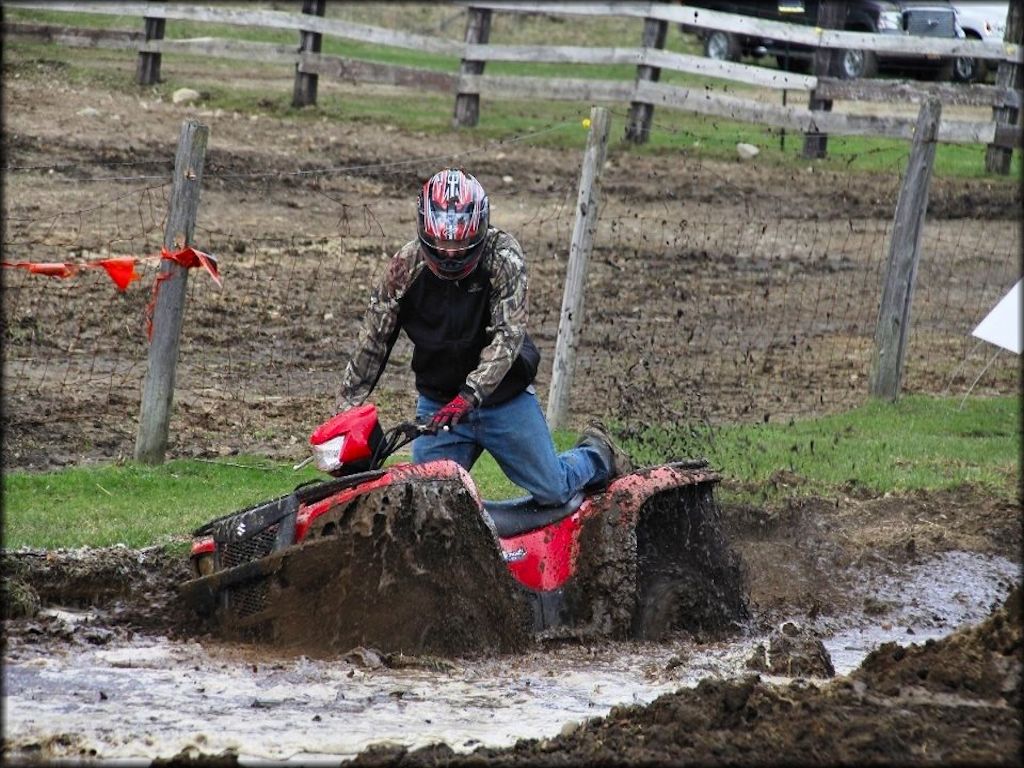 Red Suzuki ATV going through a deep mud pit.