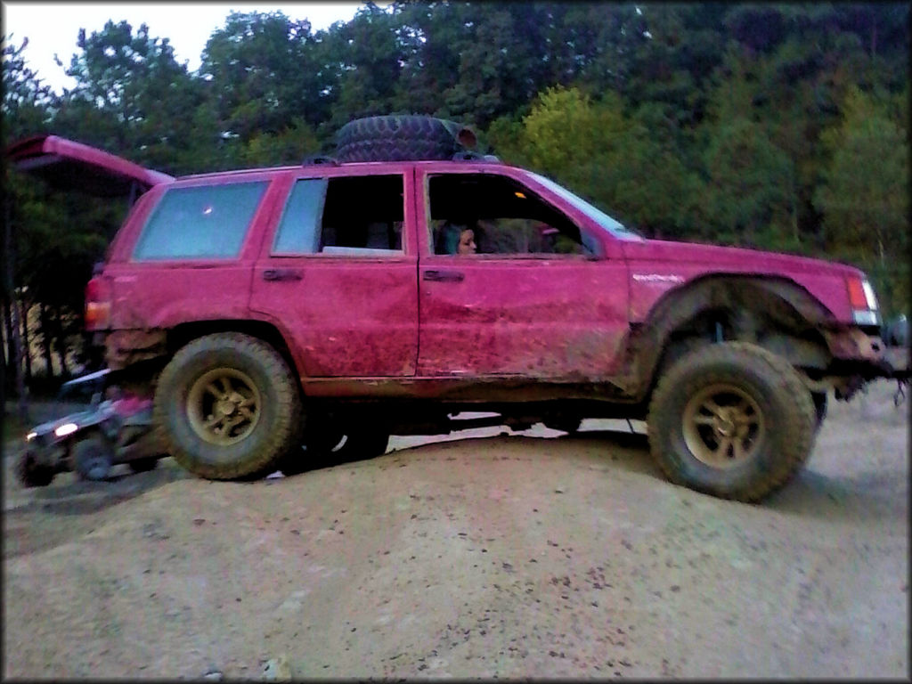 Jeep Cherokee with a spare tire on the hood and young woman sitting in passengers seat.